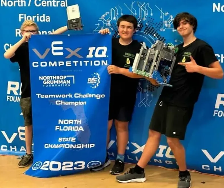 Students posing with VEX I.Q. teamwork challenge champion banner.