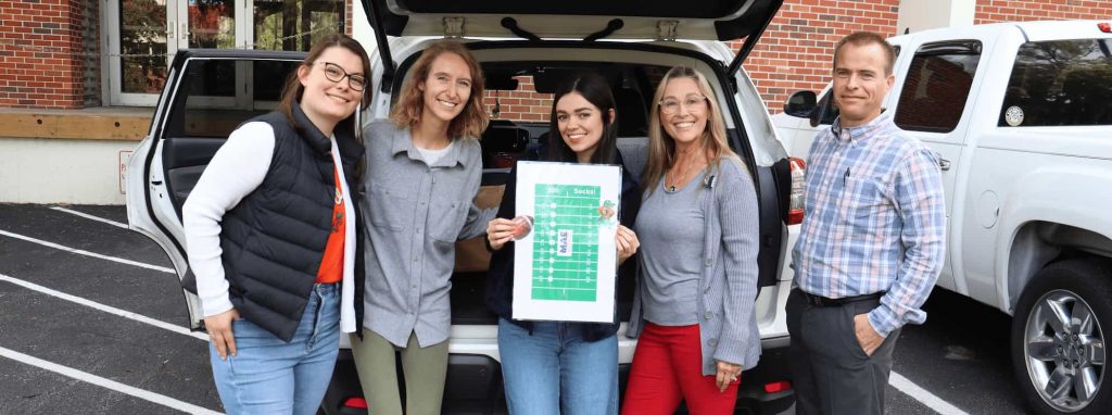 MAE team members smile while holding chart showing number of socks donated.